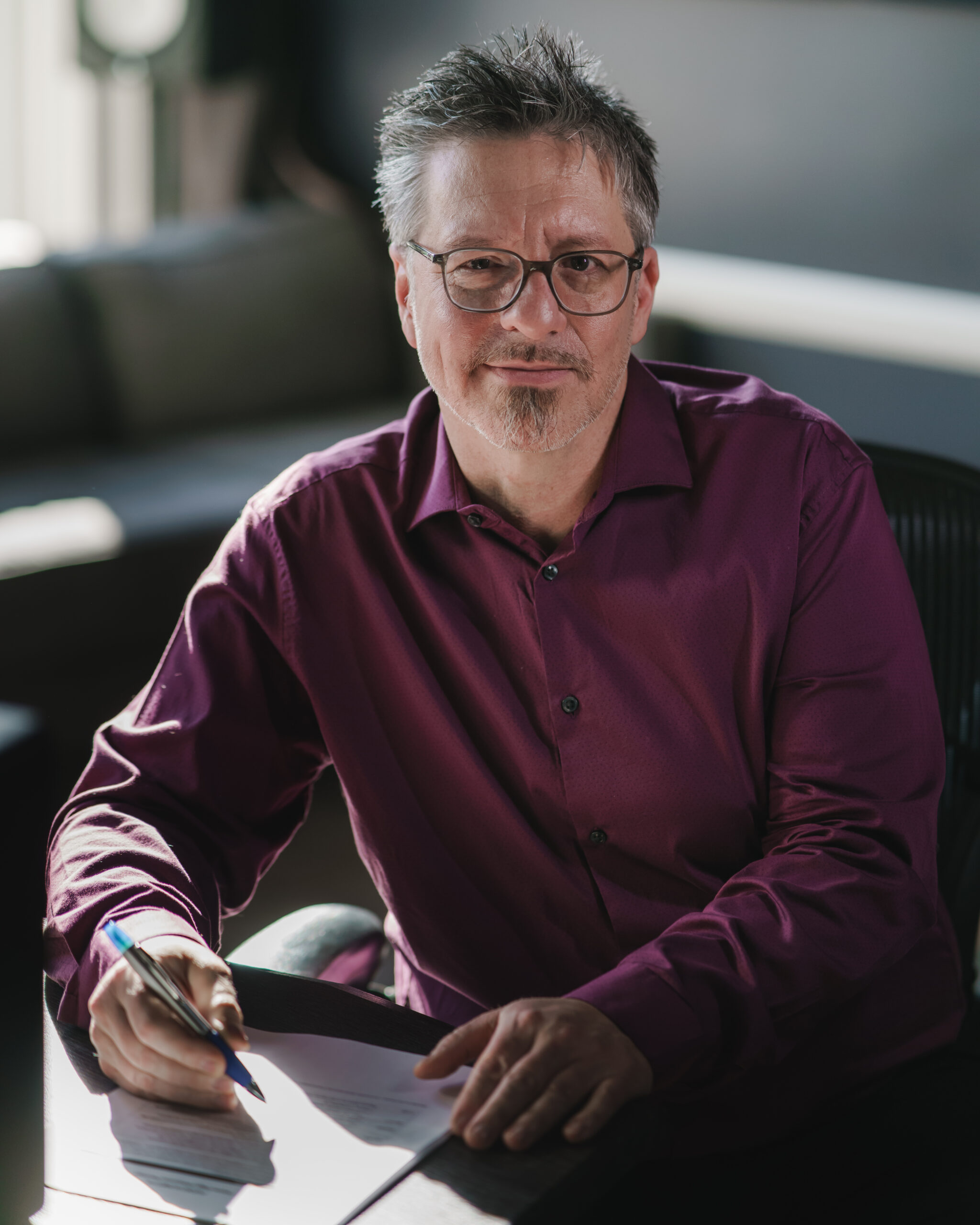 Homme assis à un bureau avec un stylo en main, en train de réviser un document, lève les yeux et sourit.