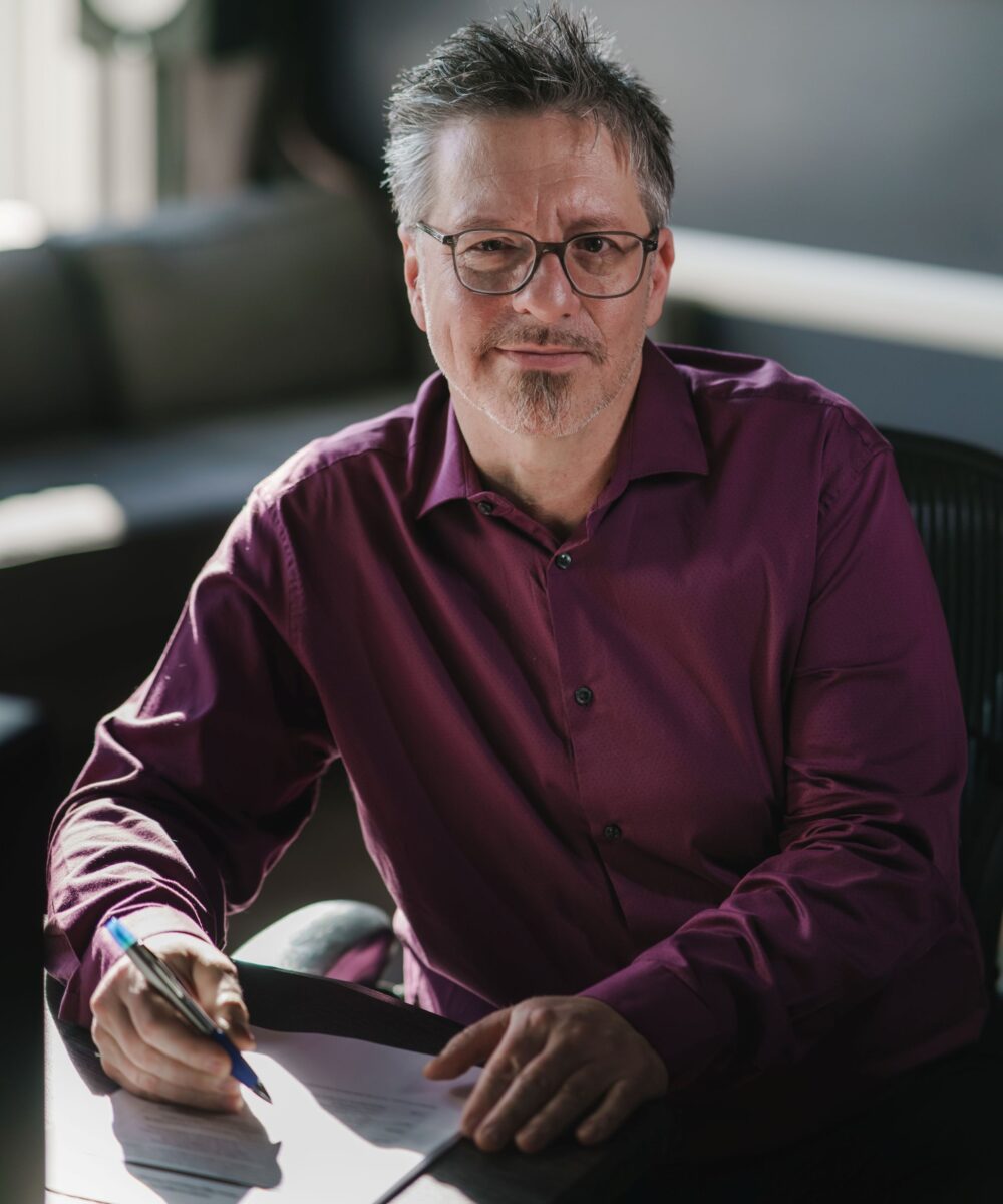 Man sitting at a desk with pen in hand reviewing a document, looks up, smiling